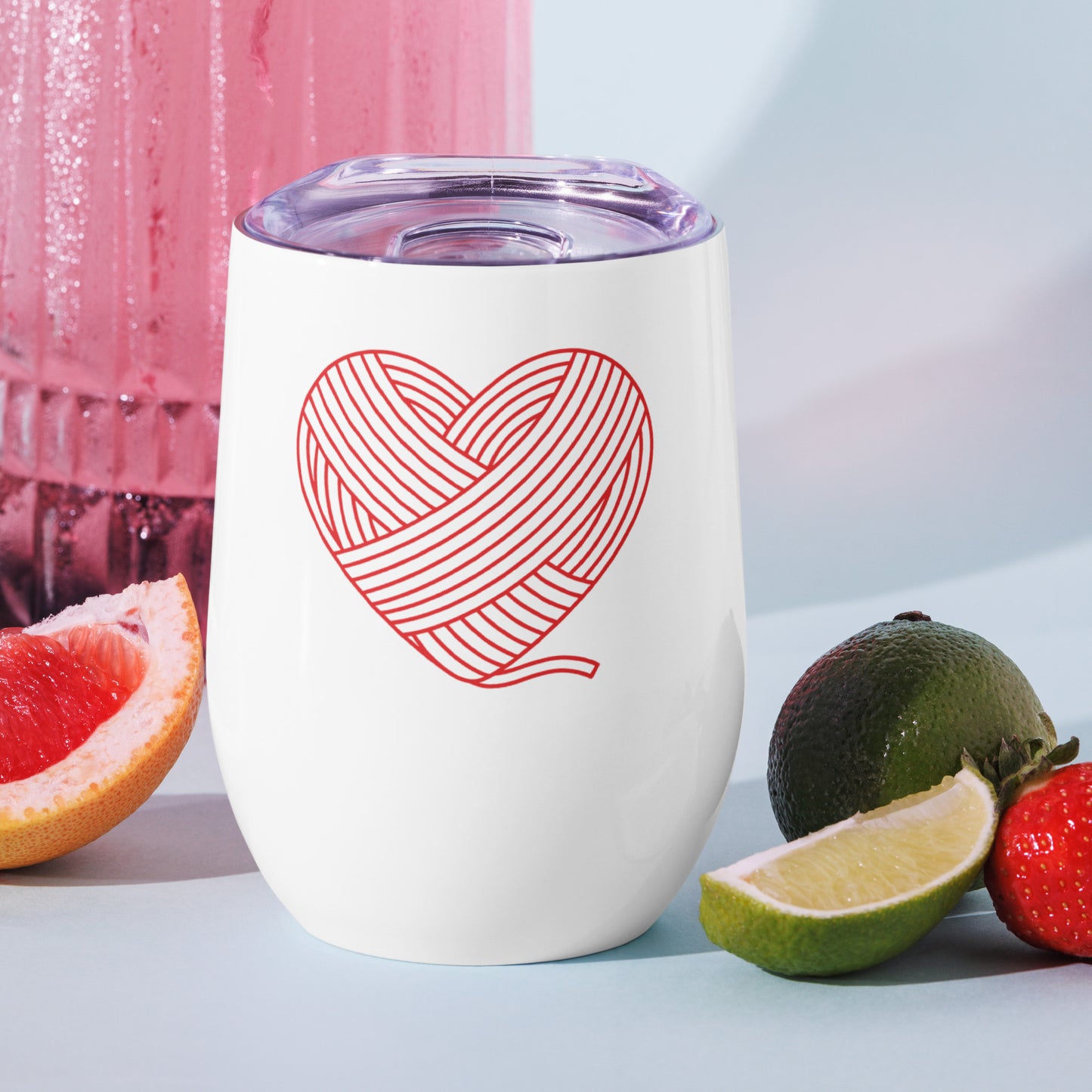 Heart Crafter stainless steel tumbler displayed beside citrus slices and a pink beverage, showing the red yarn-heart Maker Language design in a bright lifestyle setting.