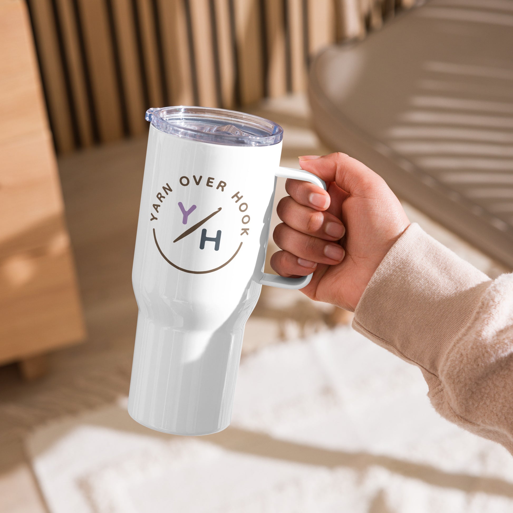 White 25 oz Yarn Over Hook travel mug with handle and clear lid held in a cozy indoor setting