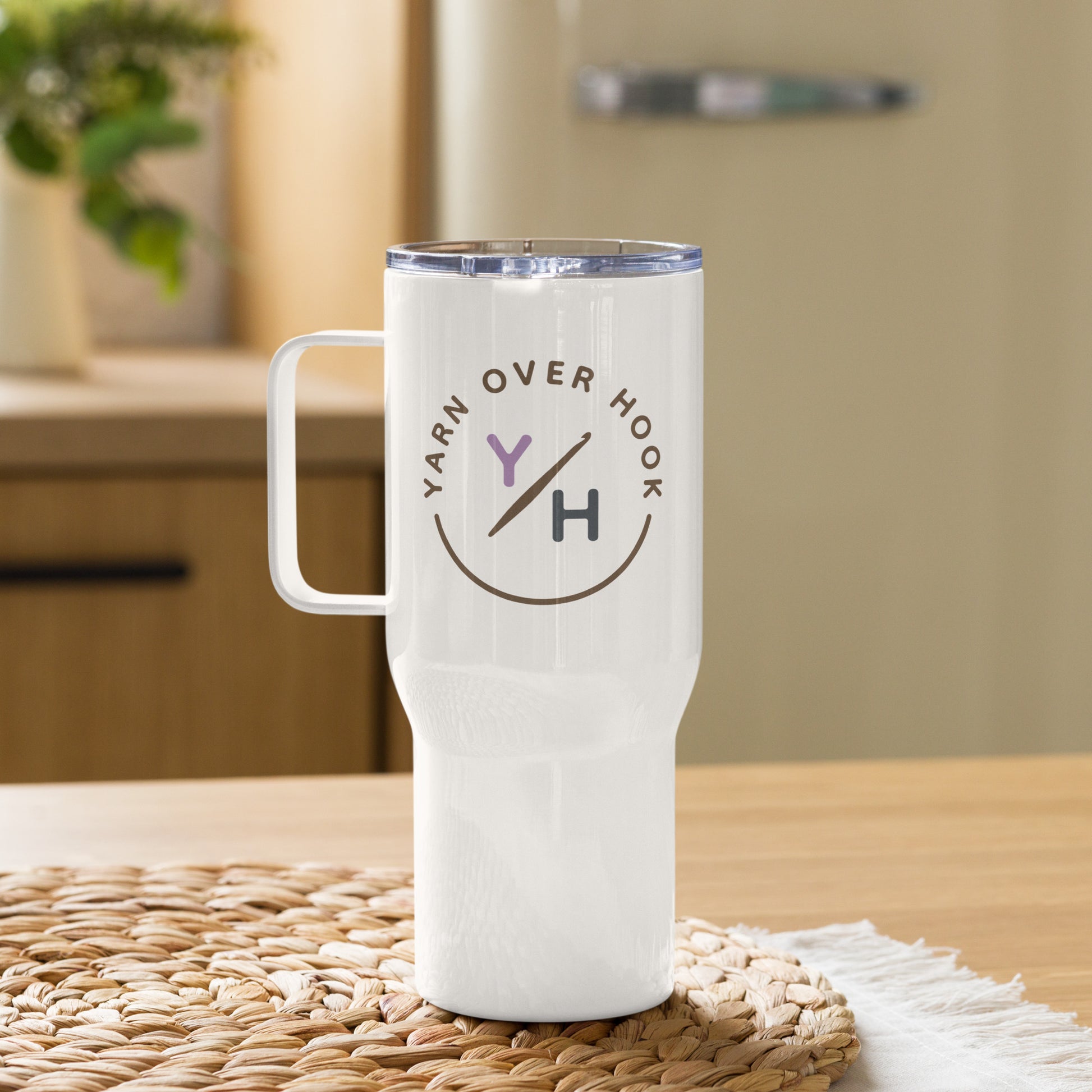White 25 oz Yarn Over Hook travel mug with handle displayed on a woven placemat
