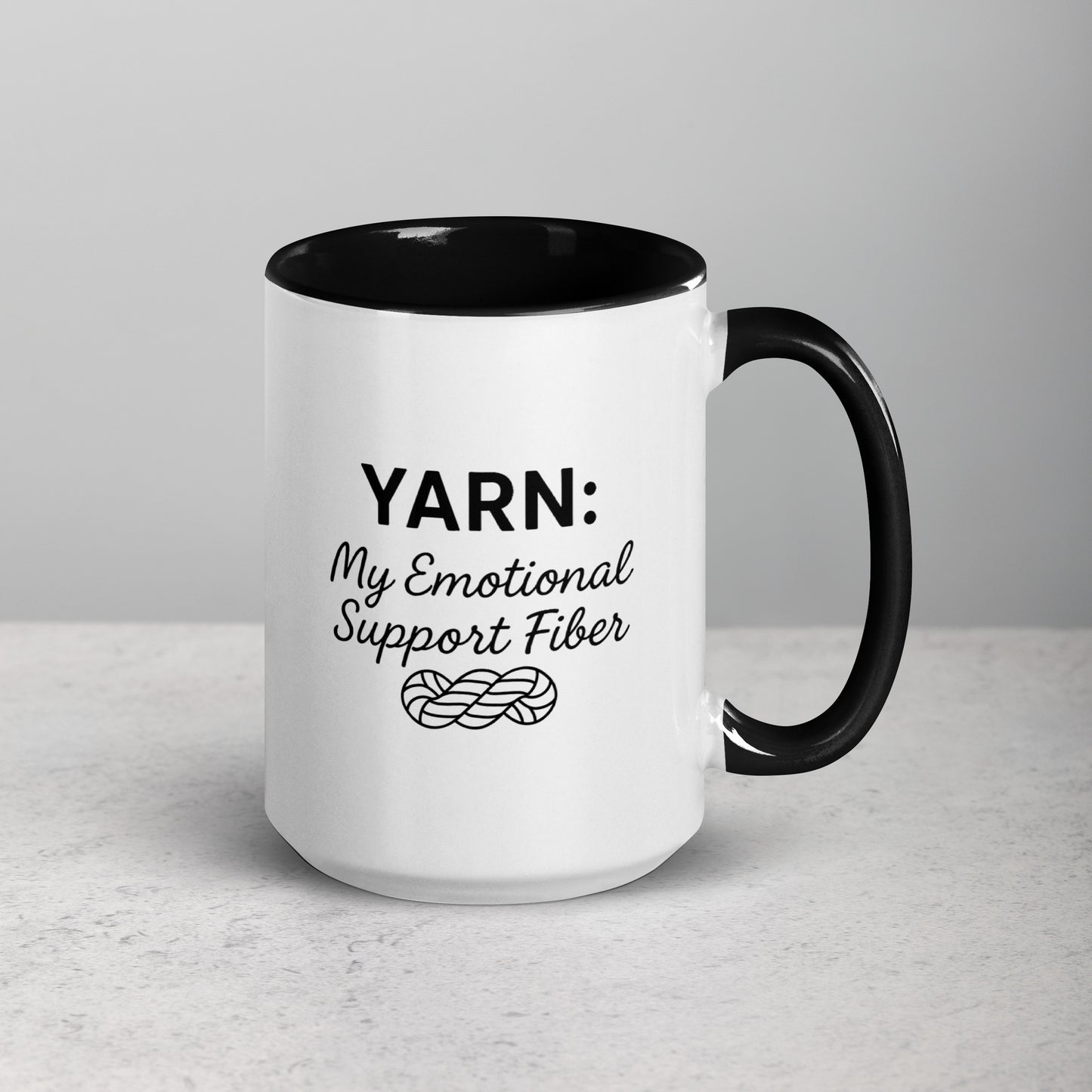 White ceramic mug with black handle and rim featuring the text “YARN: My Emotional Support Fiber” above a simple yarn illustration.