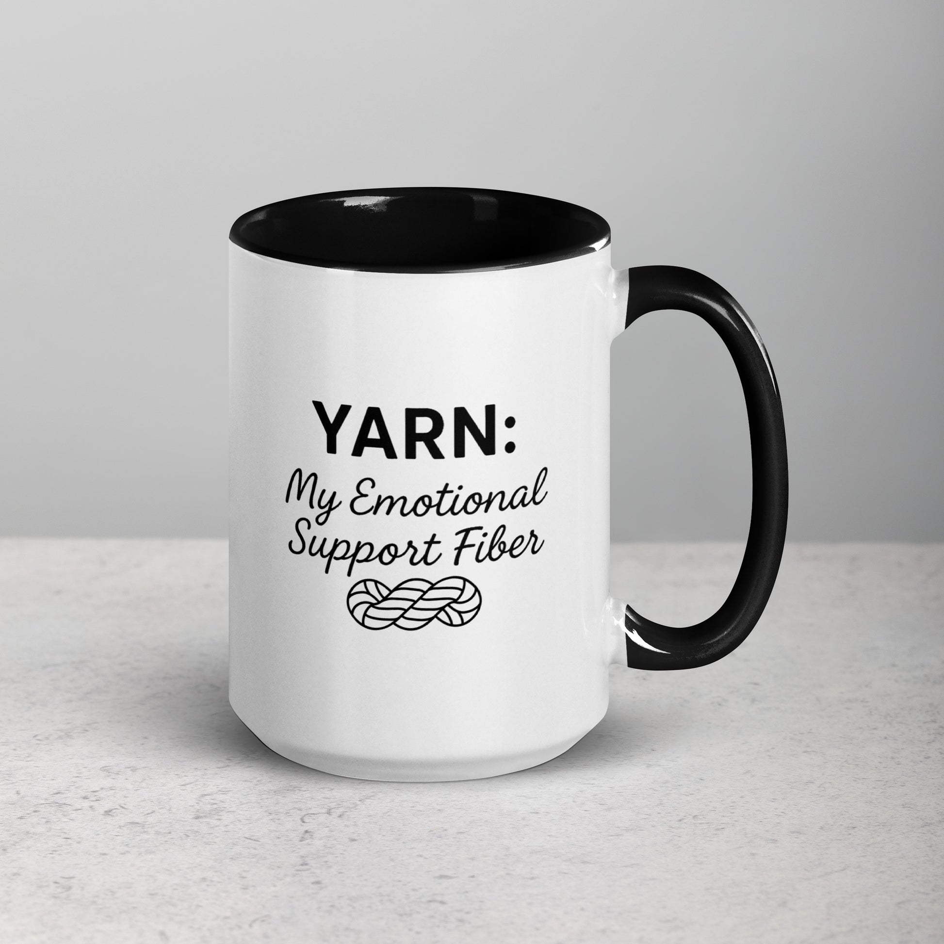White ceramic mug with black handle and rim featuring the text “YARN: My Emotional Support Fiber” above a simple yarn illustration.